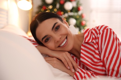 Photo of Young woman lying on bed in room with Christmas tree