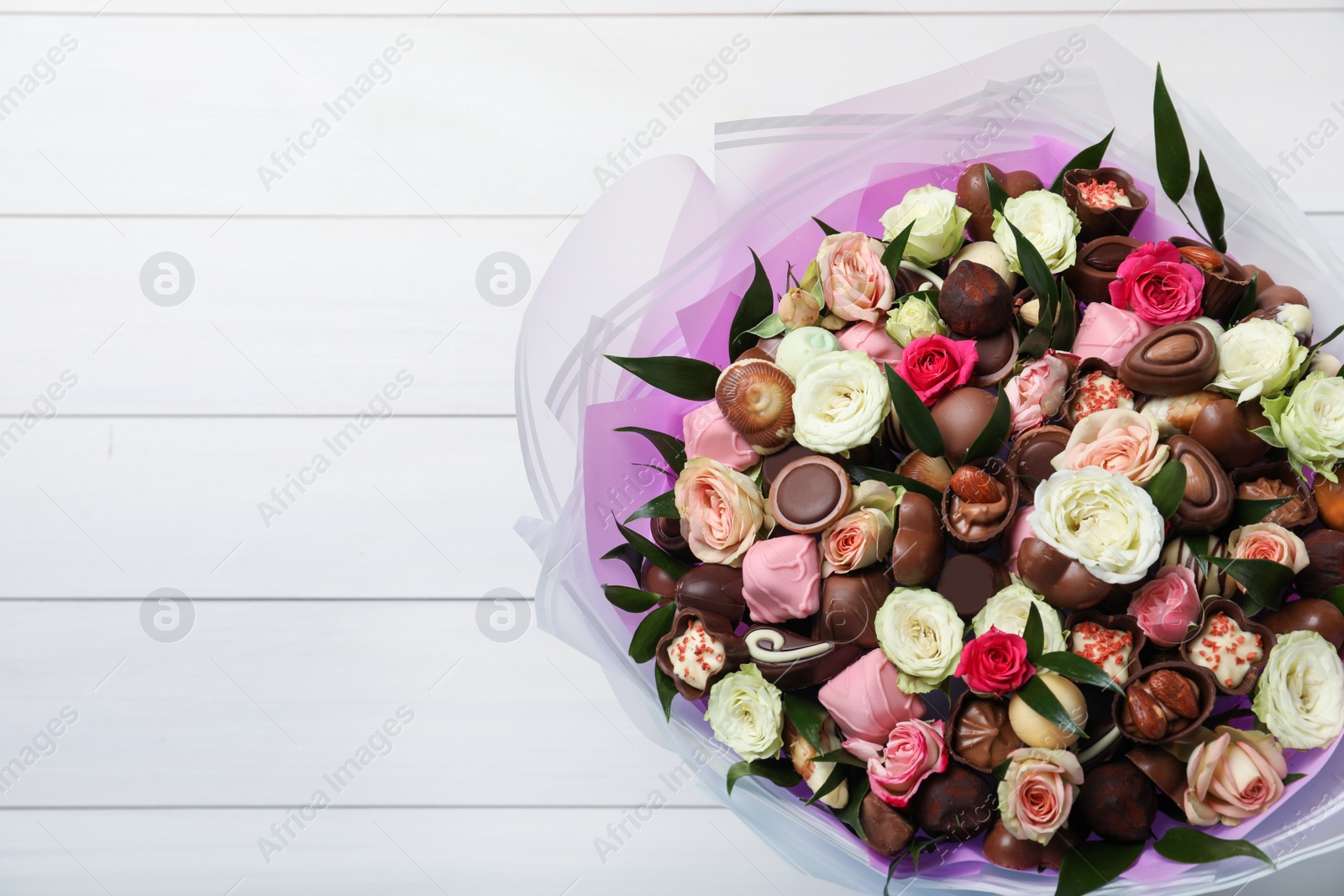 Photo of Beautiful bouquet of flowers and chocolate candies on white wooden background, top view. Space for text