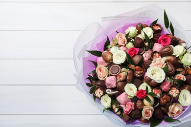 Photo of Beautiful bouquet of flowers and chocolate candies on white wooden background, top view. Space for text