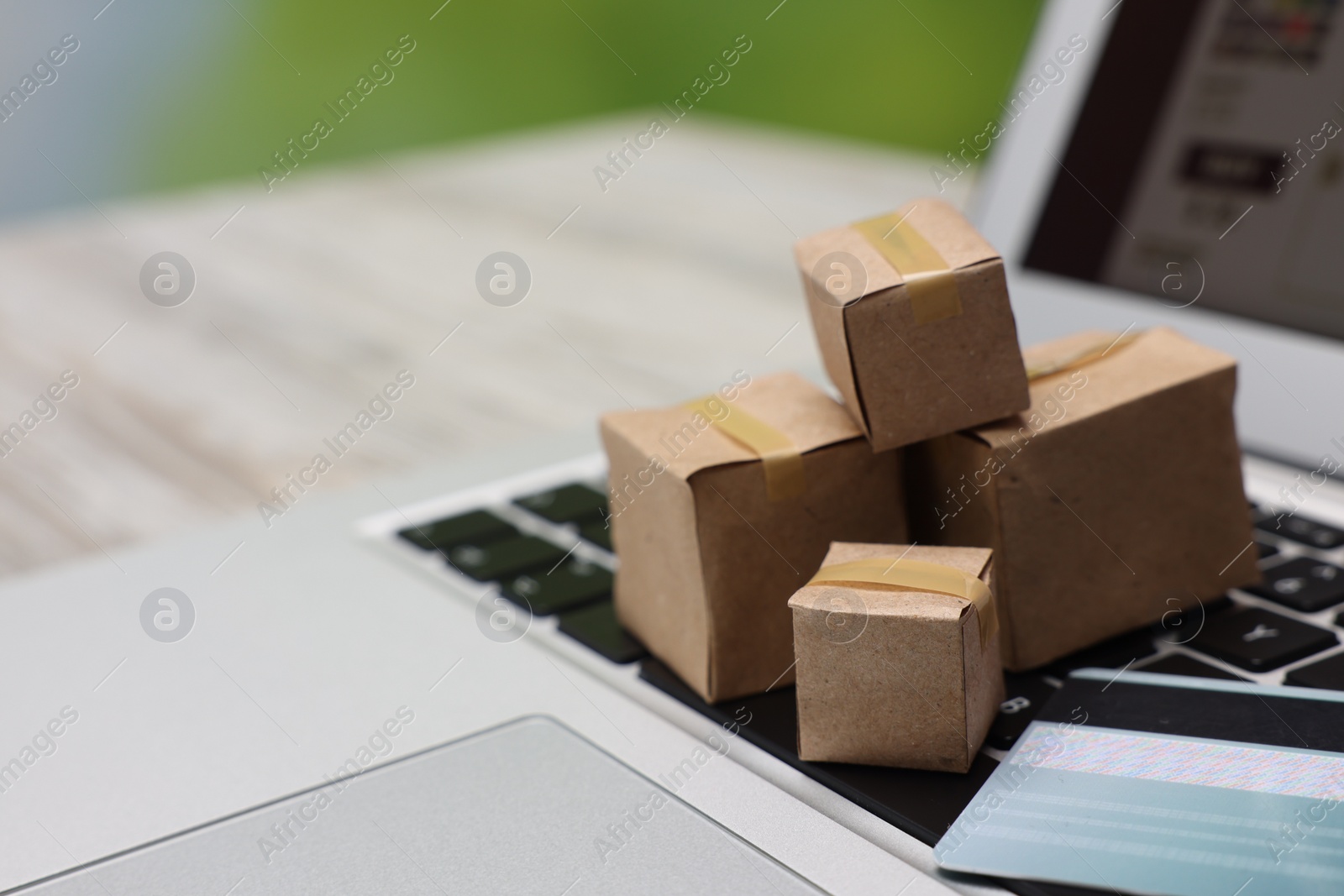 Photo of Internet shopping. Small cardboard boxes, credit card and laptop on light wooden table, closeup. Space for text