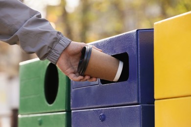 Photo of Man throwing paper coffee cup into garbage bin outdoors, closeup. Waste sorting