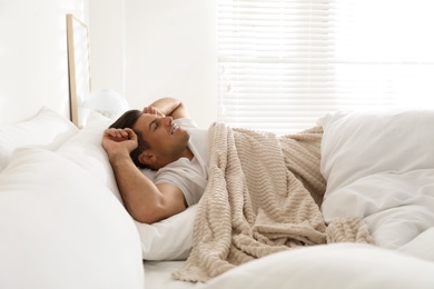 Photo of Man covered with warm beige plaid stretching in bed indoors