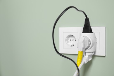 Photo of Different power plugs in socket on light green wall, closeup. Space for text