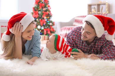 Photo of Happy couple with baby in Christmas hats at home