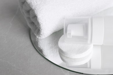 Photo of Bottle of face cleansing product, towel and cotton pads on grey table, closeup. Space for text