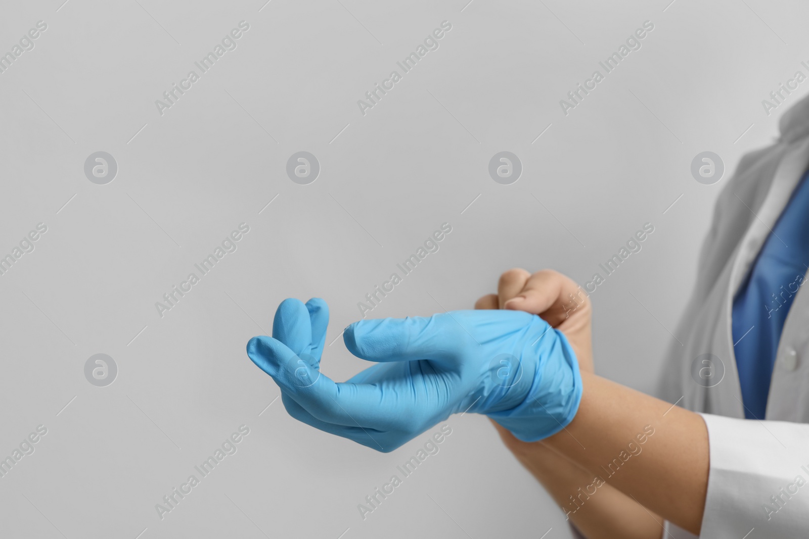 Photo of Doctor putting on medical gloves against light grey background, closeup. Space for text