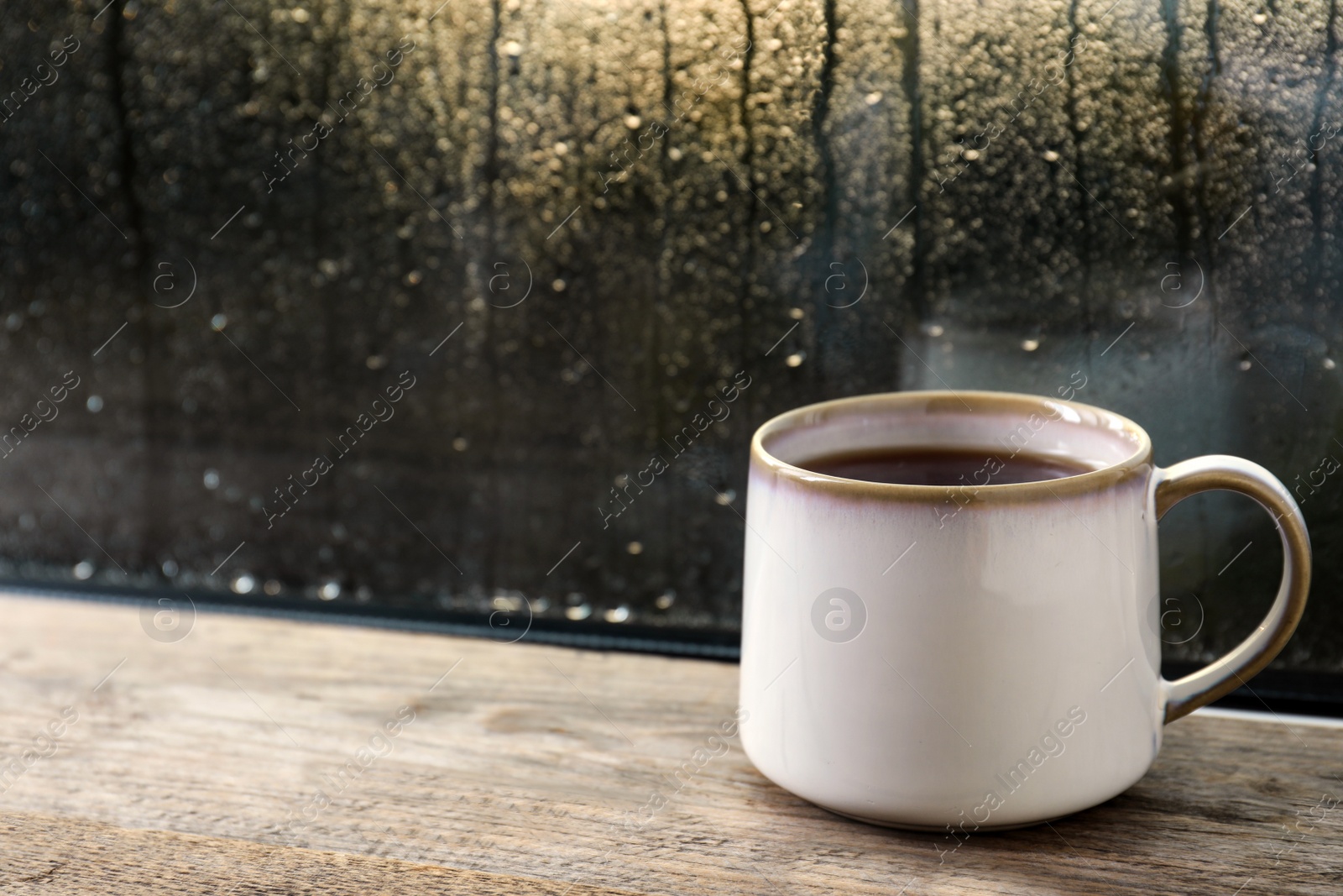 Photo of Cup of hot tea on wooden window sill. space for text. Rainy weather