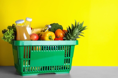 Photo of Shopping basket with grocery products on grey table against yellow background. Space for text