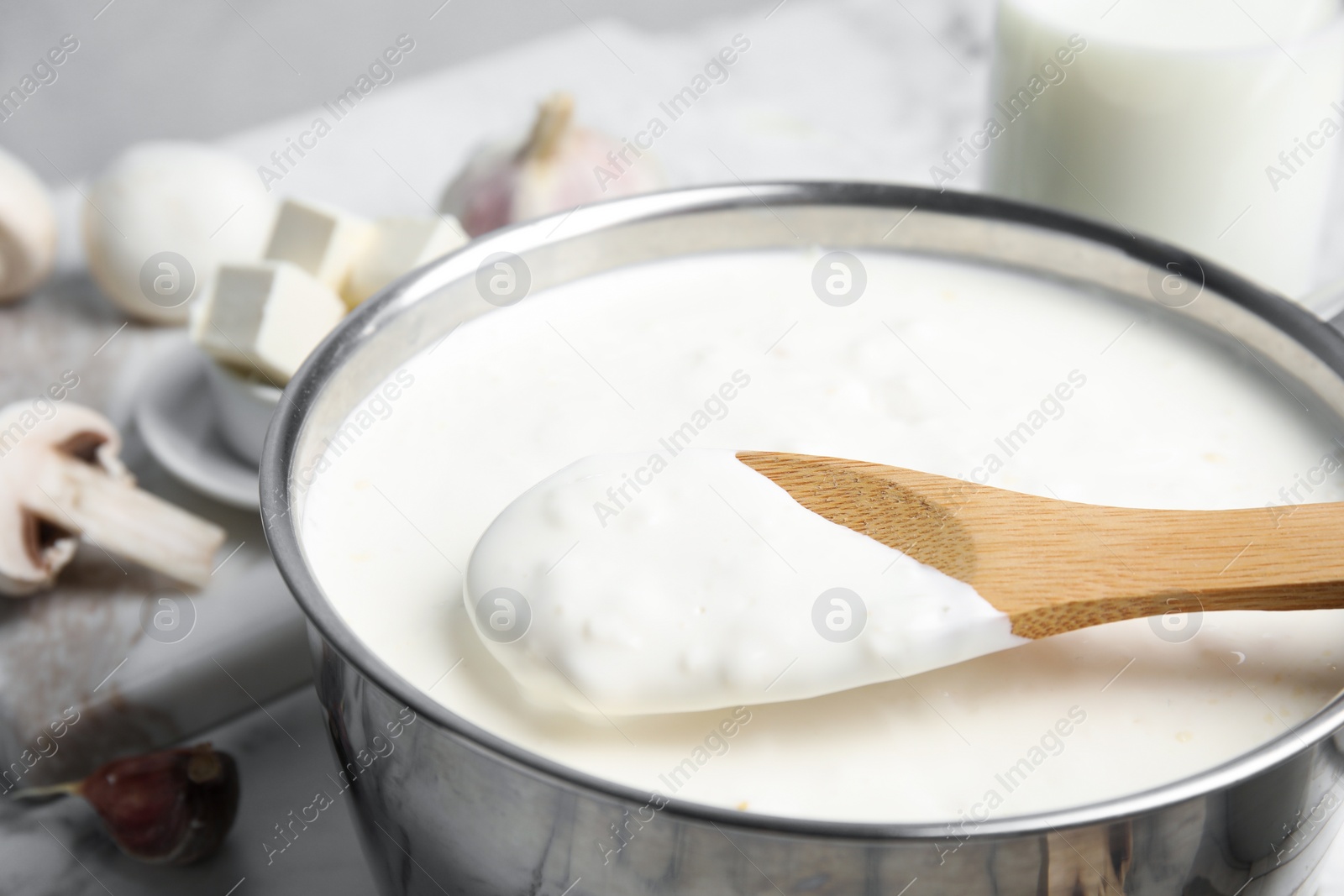 Photo of Spoon and pan with delicious creamy sauce, closeup view