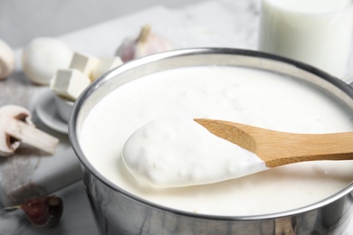 Photo of Spoon and pan with delicious creamy sauce, closeup view
