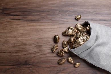 Photo of Overturned sack of gold nuggets on wooden table, flat lay. Space for text