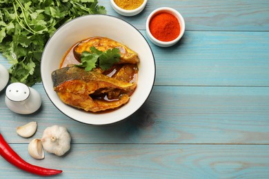 Photo of Tasty fish curry and ingredients on light blue wooden table, flat lay. Space for text. Indian cuisine