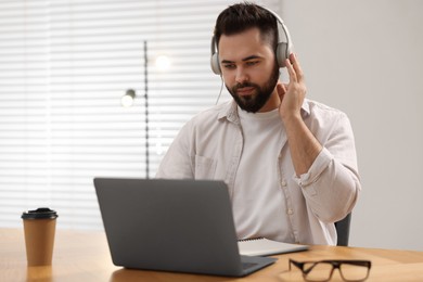 Photo of Young man in headphones watching webinar at table in room