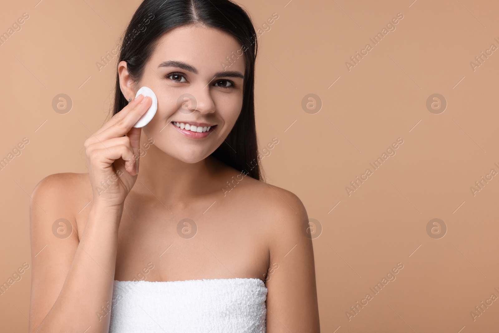 Photo of Young woman cleaning her face with cotton pad on beige background. Space for text