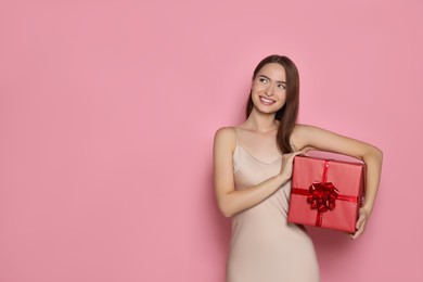 Portrait of happy young woman with gift box on pink background. Space for text