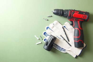 Photo of Electric screwdriver, gloves and accessories on pale green background, flat lay