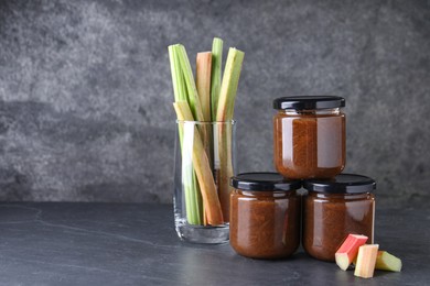 Photo of Jars of tasty rhubarb jam and stalks on grey table. Space for text