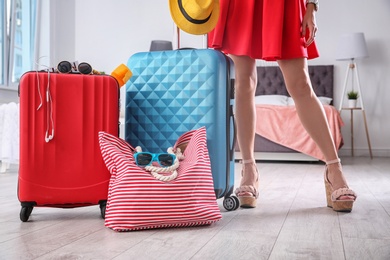 Photo of Woman standing near suitcases and bag packed for summer journey in room