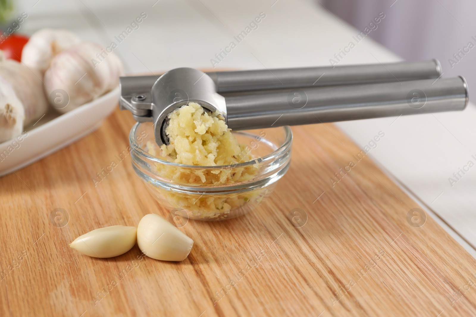 Photo of Garlic press, cloves and mince on wooden table, closeup