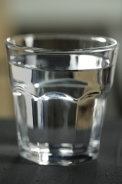 Photo of Glass of pure water on black table against blurred background, closeup