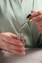 Photo of Woman with bottle of cosmetic serum at table, closeup