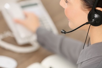 Photo of Hotline operator with headset and stationary phone working in office, closeup. Space for text