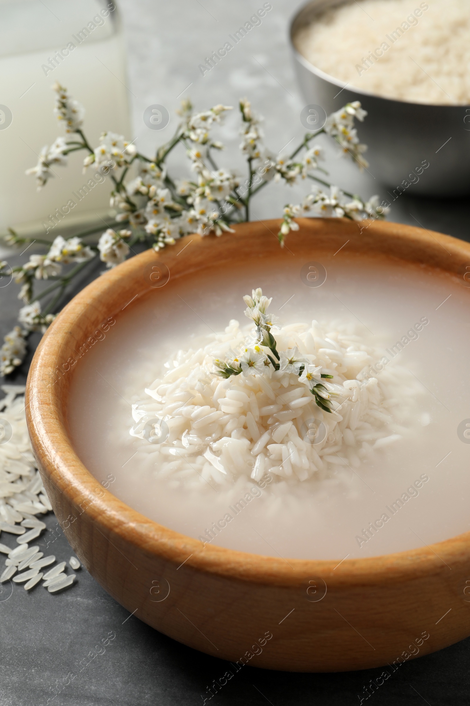 Photo of Bowl with soaked rice on grey table, closeup