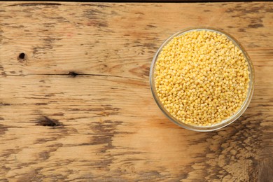 Photo of Millet groats in bowl on wooden table, top view. Space for text