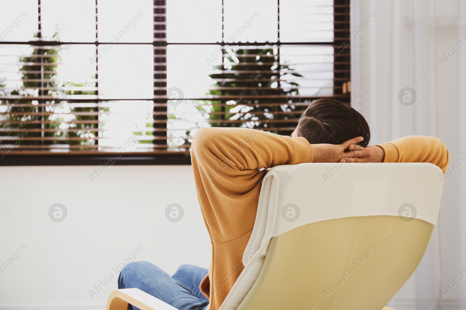 Photo of Man relaxing in armchair near window at home, back view