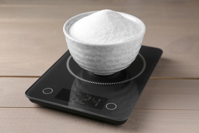 Electronic scales with sugar on light wooden table