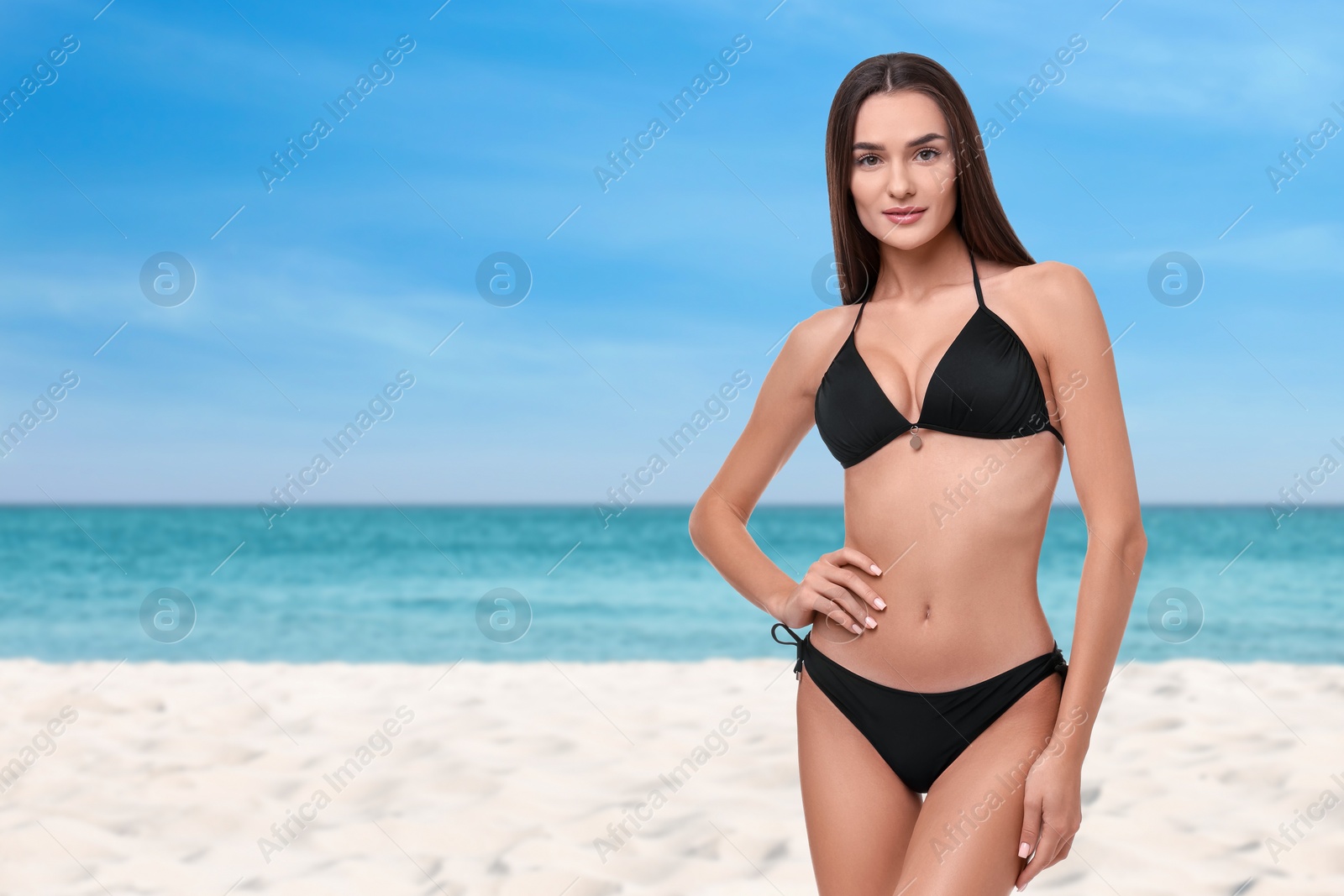 Image of Beautiful woman in stylish black bikini on sandy beach near sea, space for text