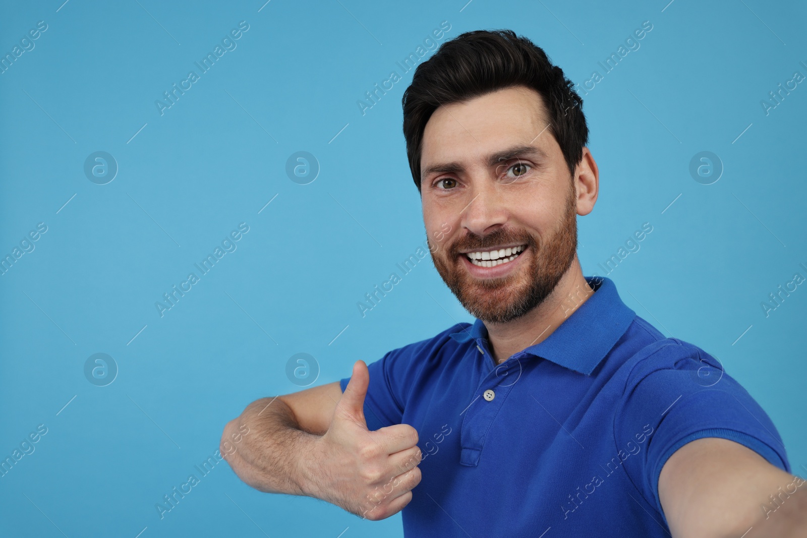 Photo of Emotional man taking selfie and showing thumbs up on light blue background, space for text