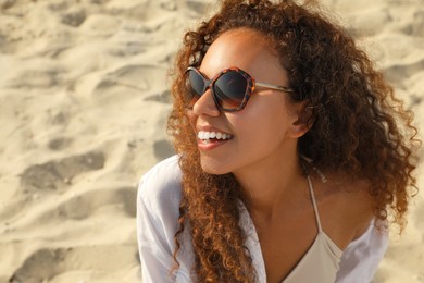 Photo of Beautiful African American woman with sunglasses at sandy beach. Sun protection care