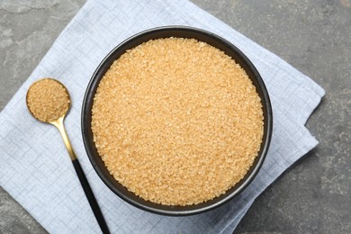 Photo of Brown sugar in bowl and spoon on grey textured table, top view