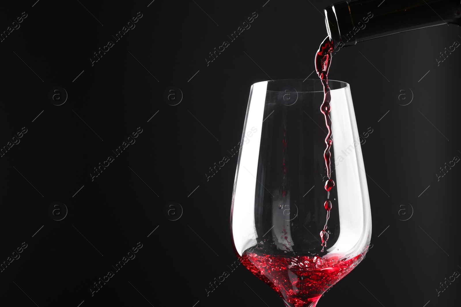 Photo of Pouring red wine into glass against black background, closeup. Space for text