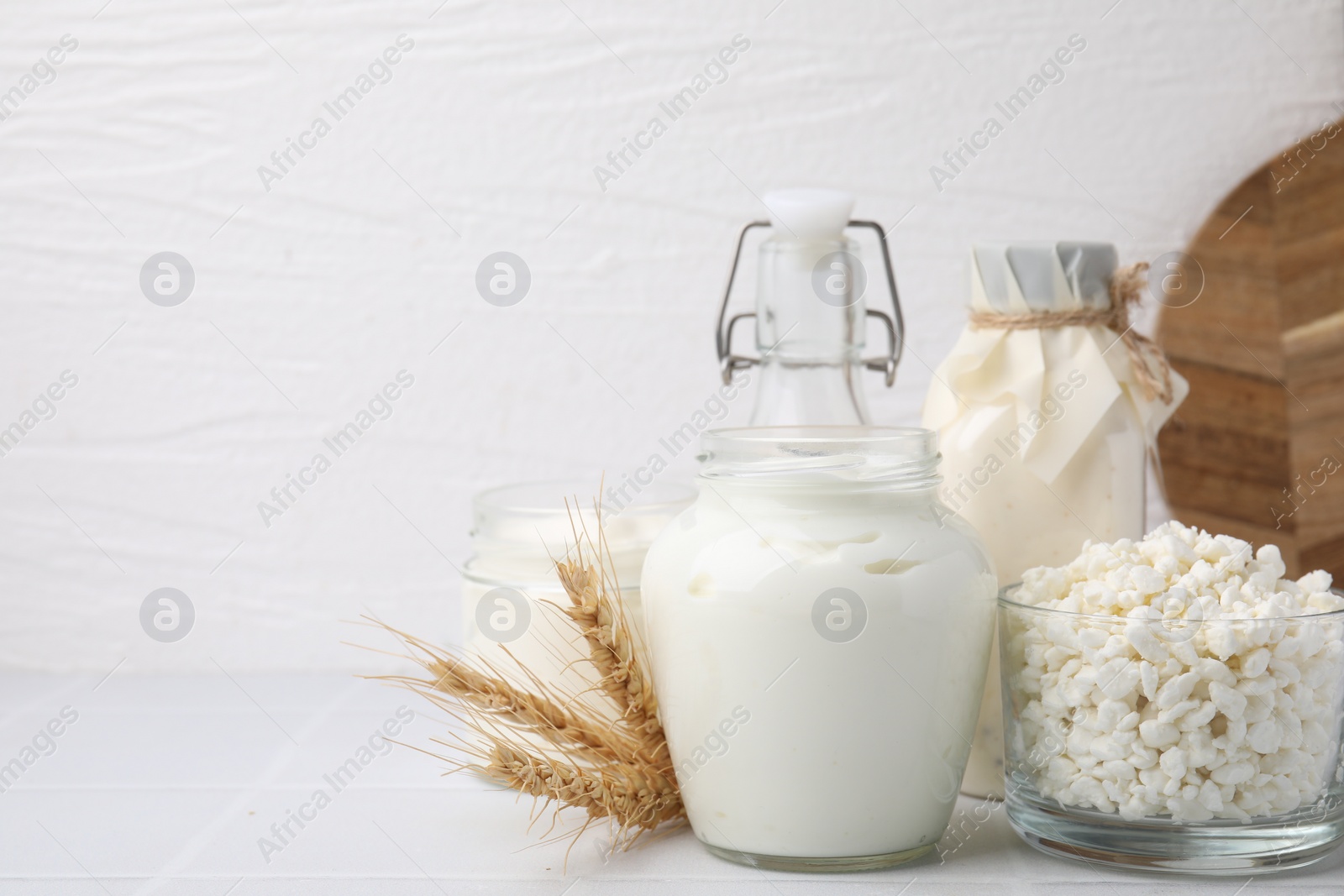 Photo of Different dairy products and spikes on white tiled table, space for text