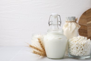 Different dairy products and spikes on white tiled table, space for text