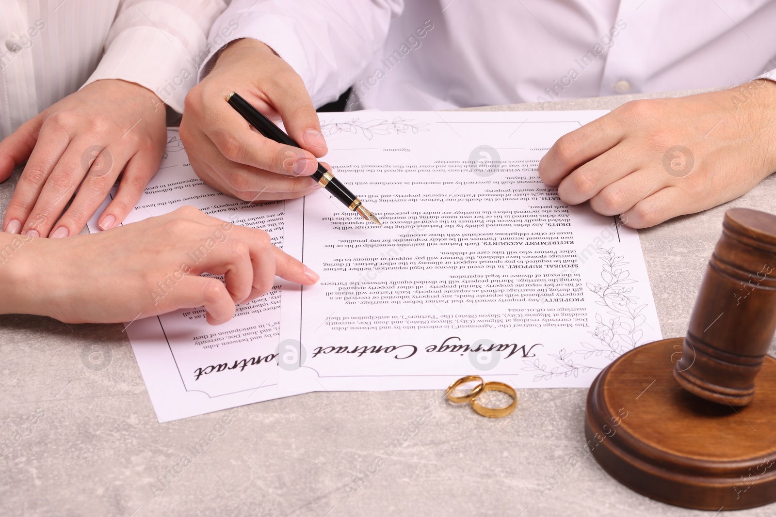 Photo of Man and woman signing marriage contract at light grey table, closeup