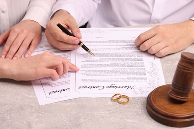 Photo of Man and woman signing marriage contract at light grey table, closeup