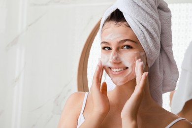 Beautiful teenage girl applying cleansing foam onto face in bathroom, space for text. Skin care cosmetic