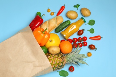 Shopping paper bag with different groceries on light blue background, flat lay