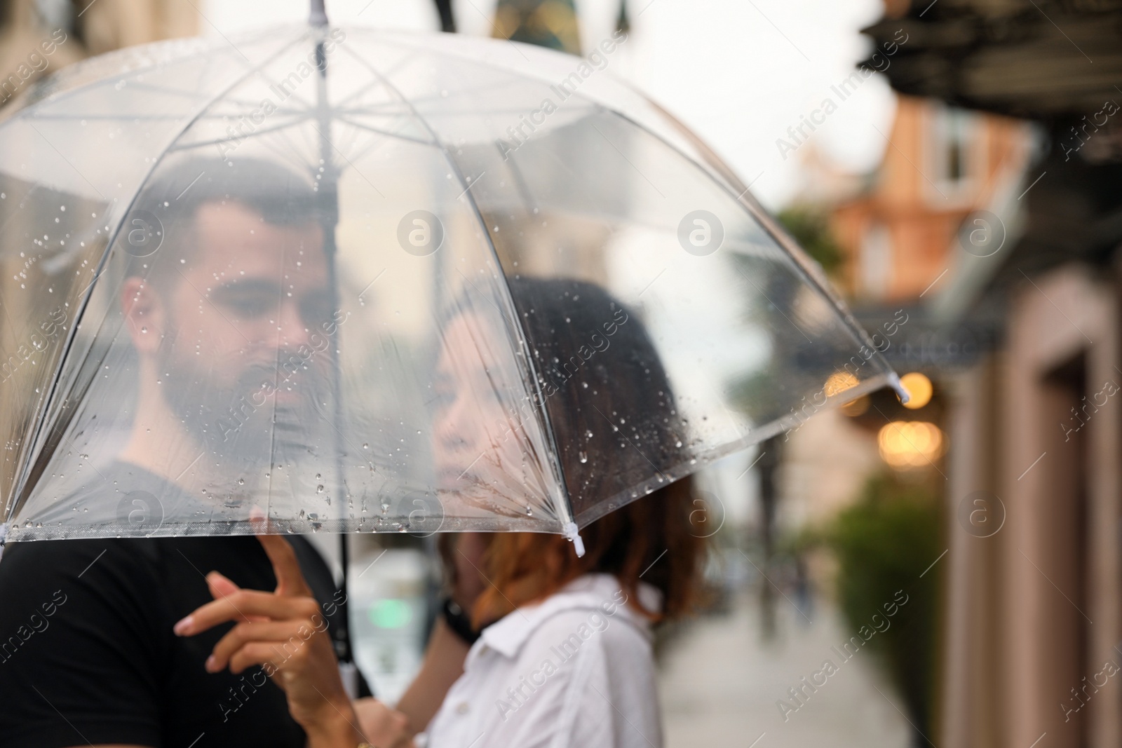 Photo of Young couple with umbrella enjoying time together under rain on city street