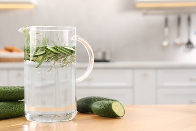 Photo of Refreshing cucumber water with rosemary in jug and vegetable on wooden table. Space for text