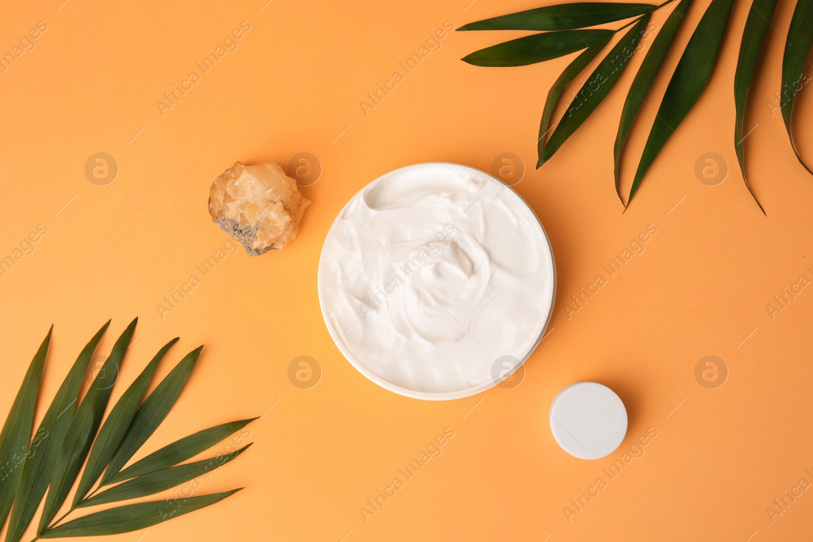 Photo of Cosmetic products, quartz gemstone and palm leaves on orange background, flat lay