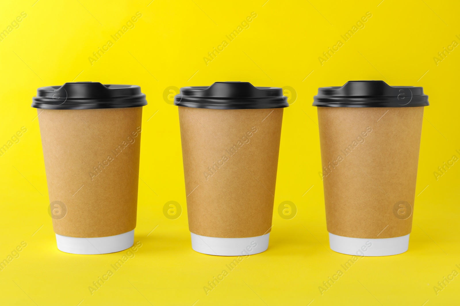 Photo of Paper cups with black lids on yellow background. Coffee to go