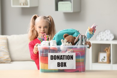 Photo of Cute little girl holding donation box with toys at home