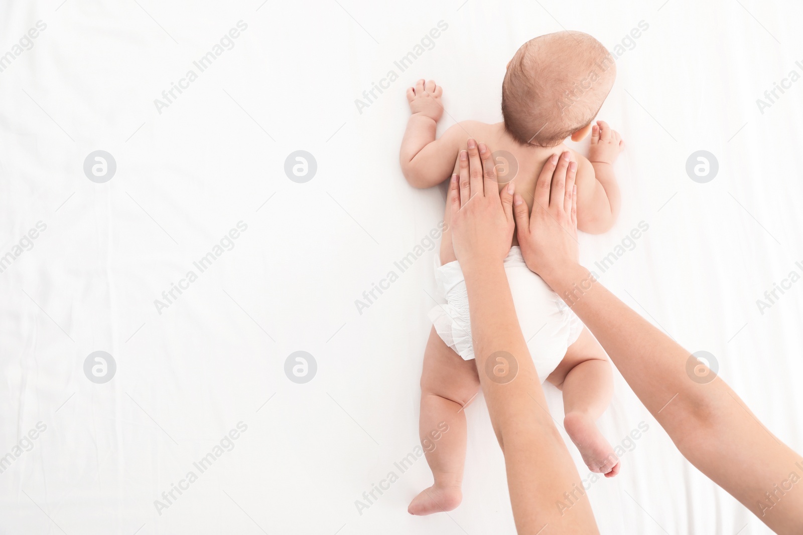 Photo of Top view of mother and her cute child on white bed, space for text. Baby massage and exercises