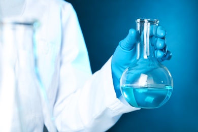 Photo of Scientist holding Florence flask with liquid on color background, closeup. Solution chemistry
