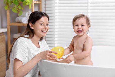 Photo of Mother bathing her cute little baby in tub at home