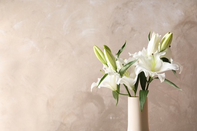 Vase with beautiful lilies on light brown background, space for text